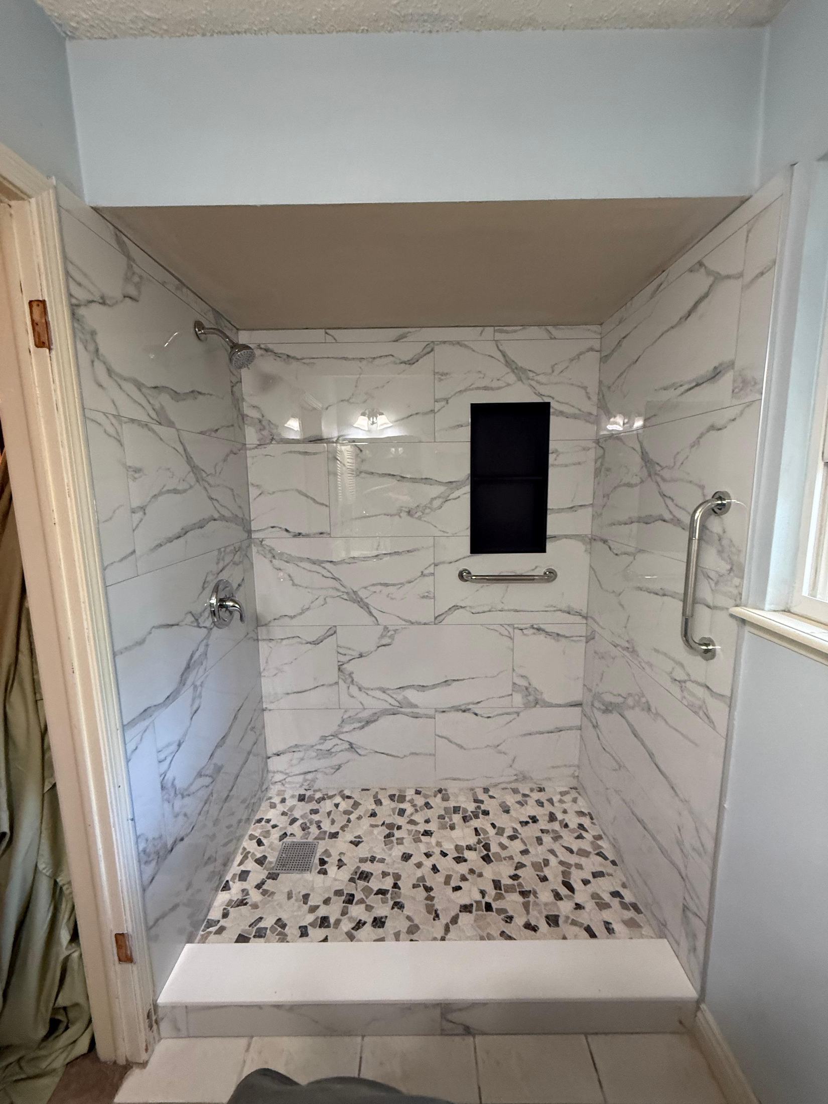 Finished shower with marble-look tile, niche and grab bars